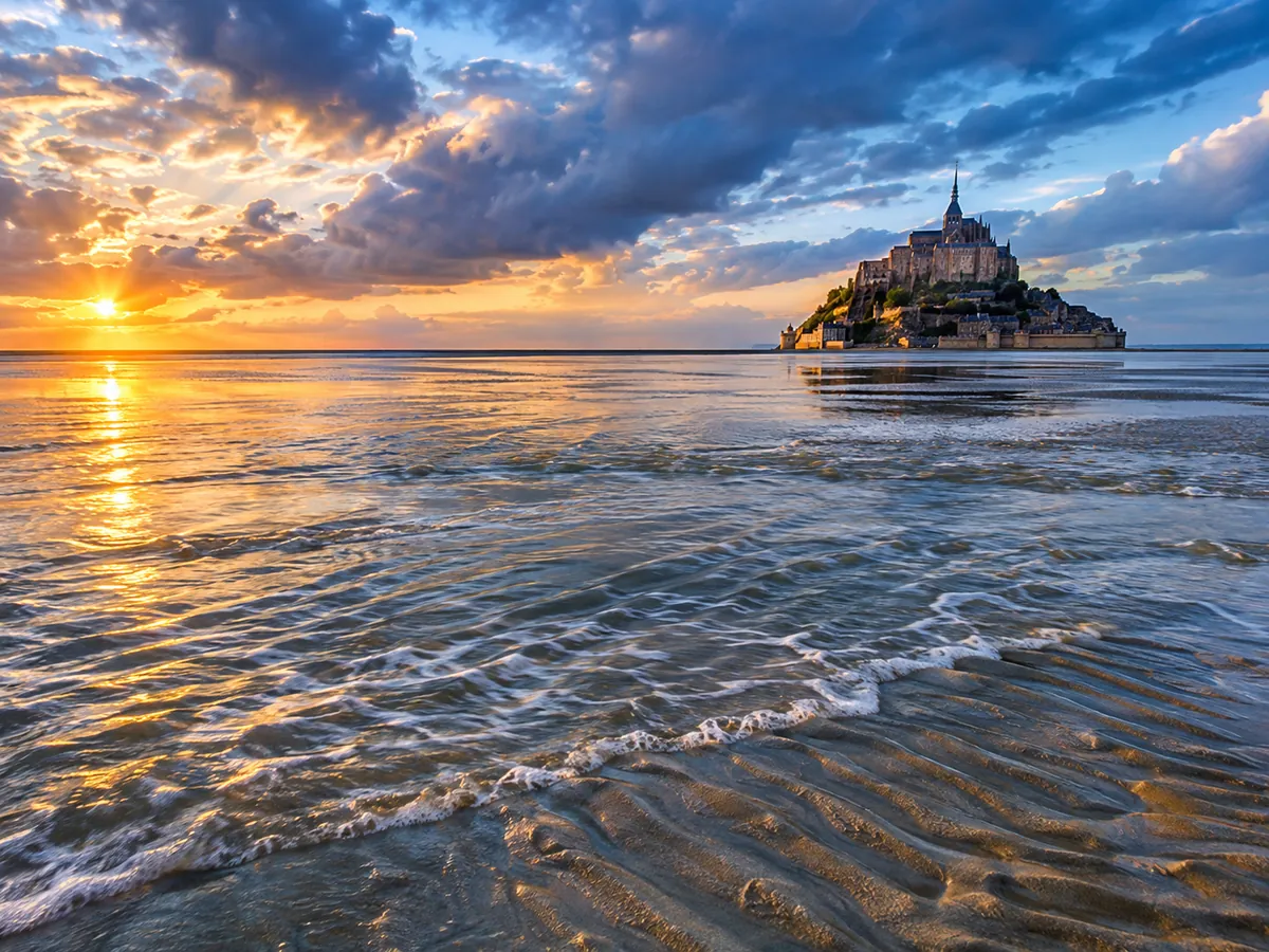 Die Flut, die über den gewellten Sand der Bucht strömt, mit der Abtei-Insel in der Ferne